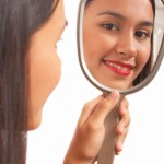 Teen girl looking at self in the mirror.