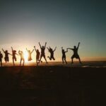 group of people jumping up with joy on a beach with a sunset.