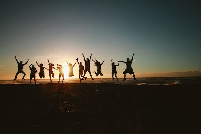 group of people jumping up with joy on a beach with a sunset.